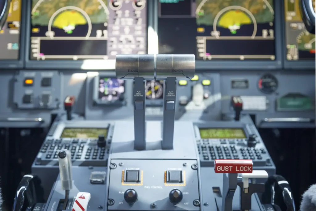 Close-up of the Gulfstream G550 SN:5562 throttle quadrant and fuel control panel, with labeled thrust levers, navigation screens in the background, and a visible red gust lock lever.