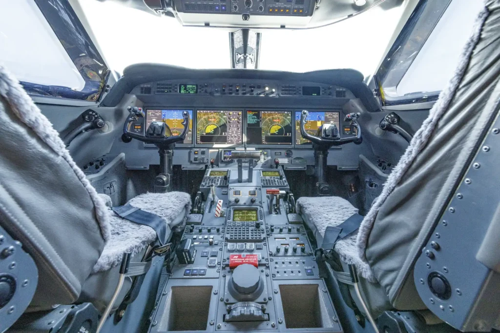 Full cockpit view of Gulfstream G550 SN:5562, showing twin pilot seats with plush grey covers, four primary flight displays, dual yokes, and an extensive center console of avionics and flight controls.