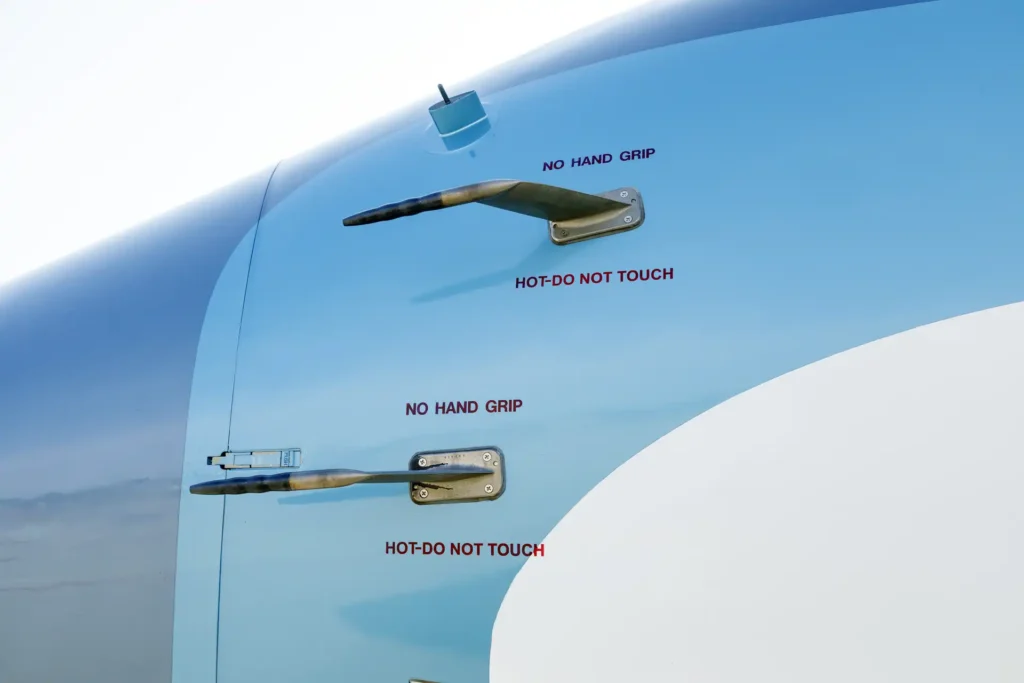 Close-up of nose probes on Gulfstream G550 SN:5562, labeled with red safety warnings: “NO HAND GRIP” and “HOT - DO NOT TOUCH,” mounted on the sky-blue fuselage.