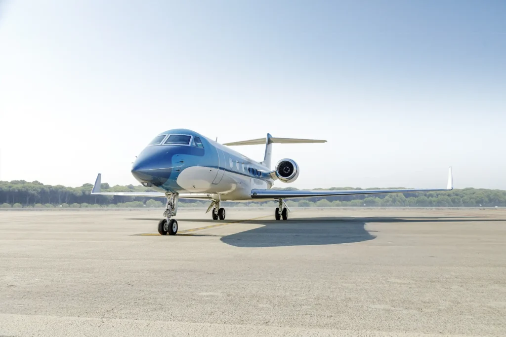 Wide front-left runway view of Gulfstream G550 SN:5562, tail number OE-LCZ, surrounded by open tarmac and casting a bold shadow beneath its sleek frame.