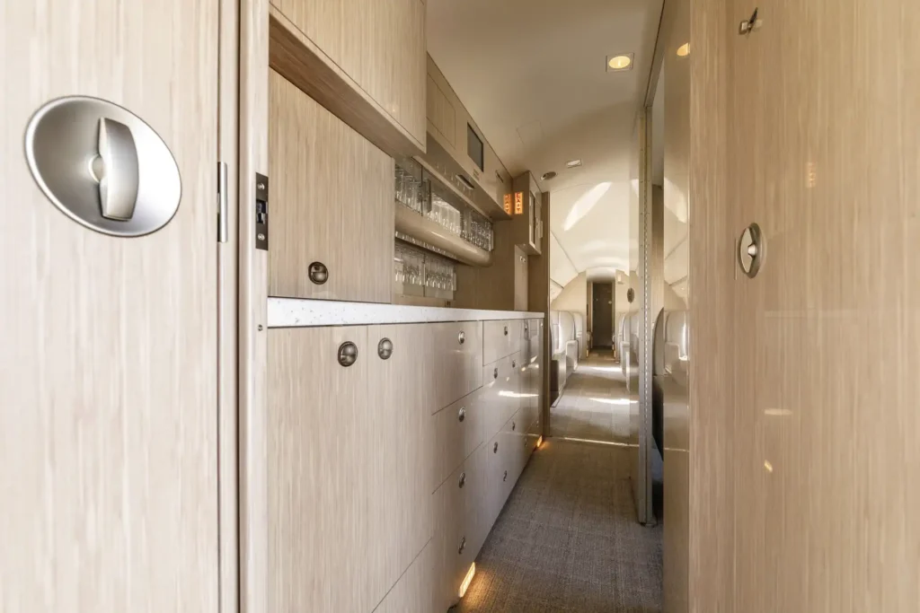 Closer shot of the aircraft galley inside Gulfstream G550 SN:5562, featuring glossy wood drawers, overhead glassware storage, and ambient lighting along the floor.