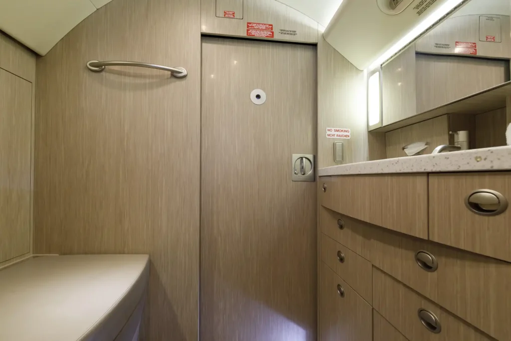 Lavatory interior aboard Gulfstream G550 SN:5562, featuring a curved leather seat, sleek vanity with storage drawers, and mirrored cabinetry under soft lighting.